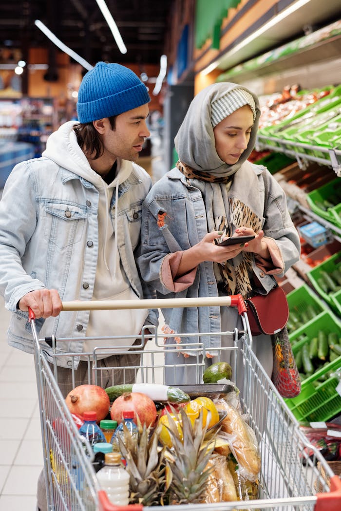 A couple in a supermarket selecting groceries with a shopping cart full of fresh produce.